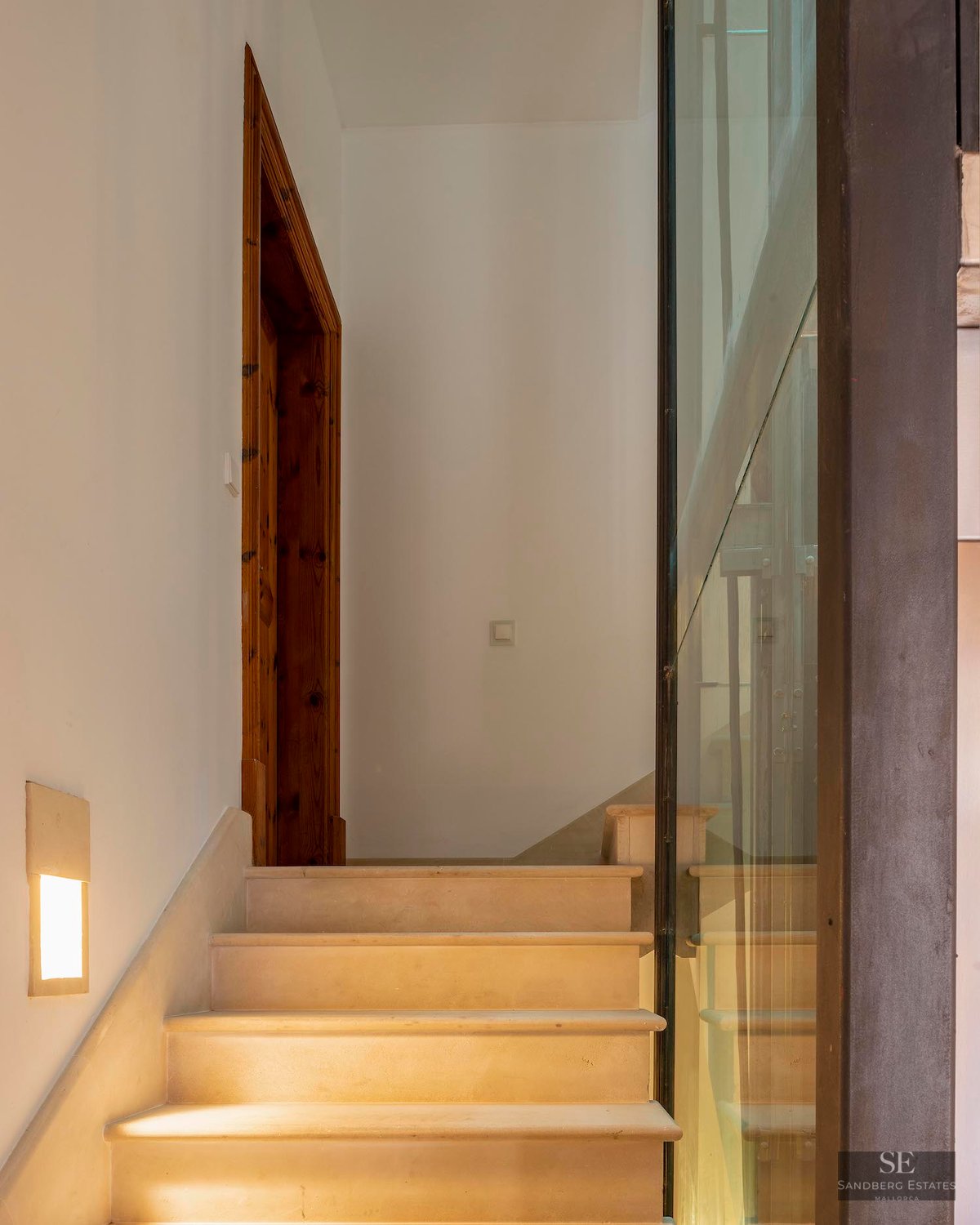 Stone steps leading up next to a glass wall and wooden door frame, illuminated by warm wall lights.