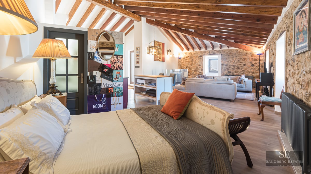 Luxury bedroom featuring exposed wooden beams, natural stone walls, and an integrated living area.