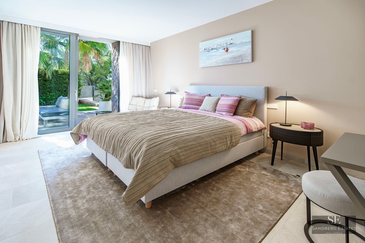 Chambre moderne avec grand lit, lampes design et baies vitrées ouvrant sur une terrasse de jardin luxuriante.