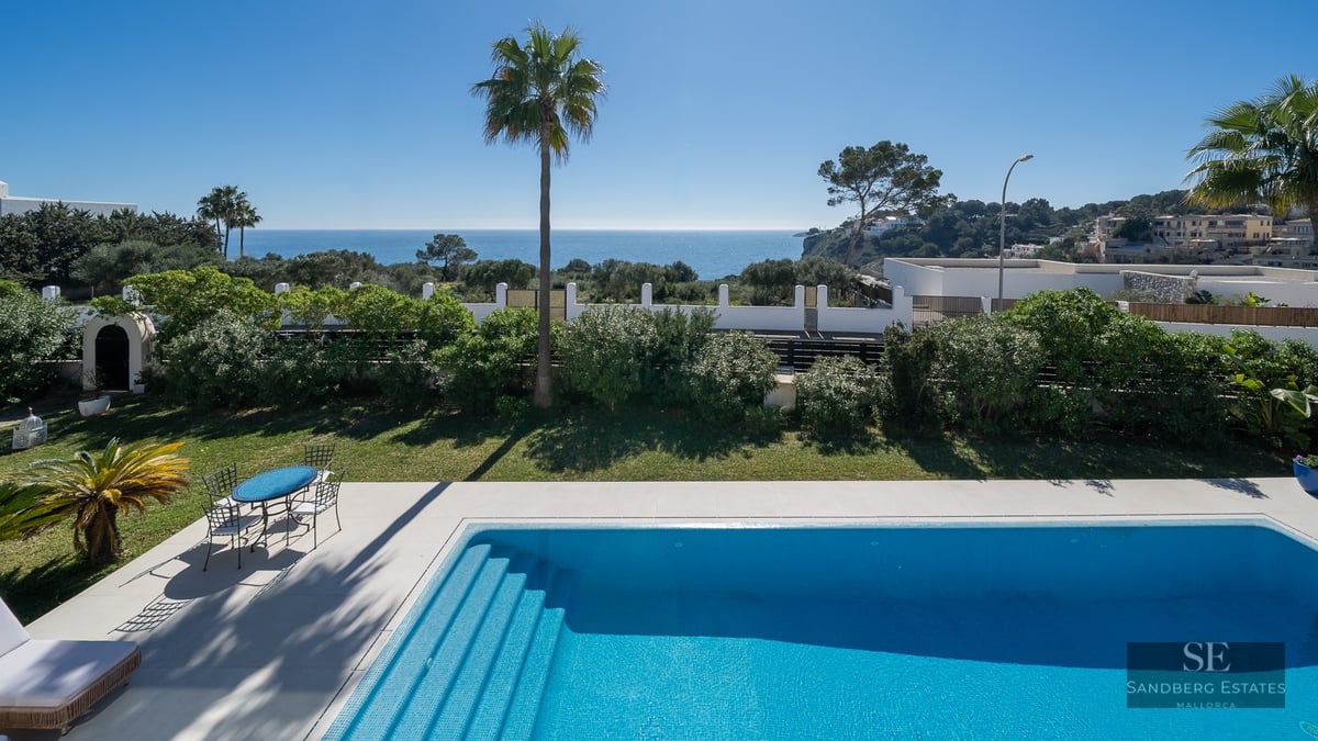 A blue tiled swimming pool and garden area overlooking the Mediterranean Sea under a clear blue sky.
