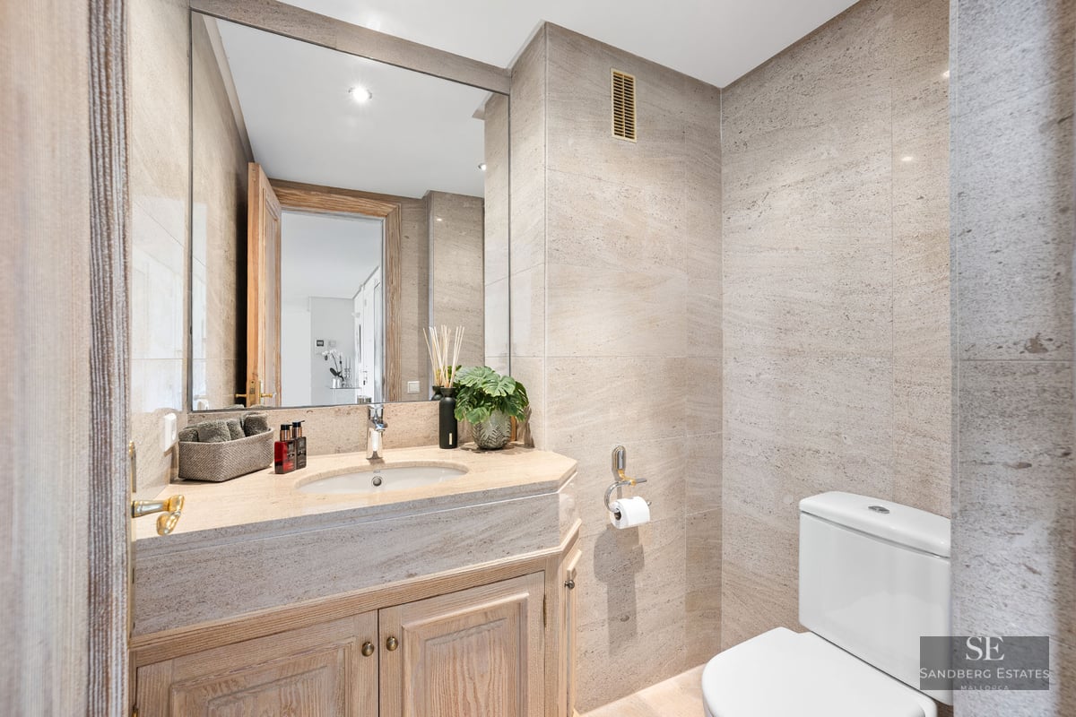 Salle de bains moderne avec carrelage en pierre beige, grand miroir et meuble sous vasque en bois.