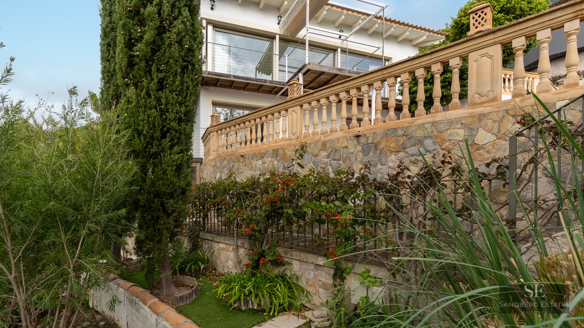 Tiered garden with stone retaining walls, classic balustrades, and lush cypress trees leading to a white villa.