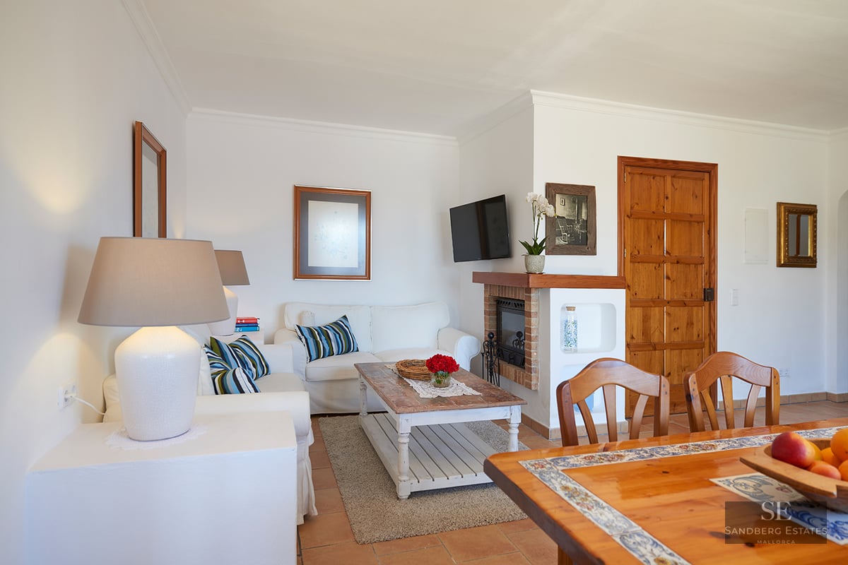 Bright living room with white sofas, a rustic wooden coffee table, a fireplace, and terracotta tile flooring.