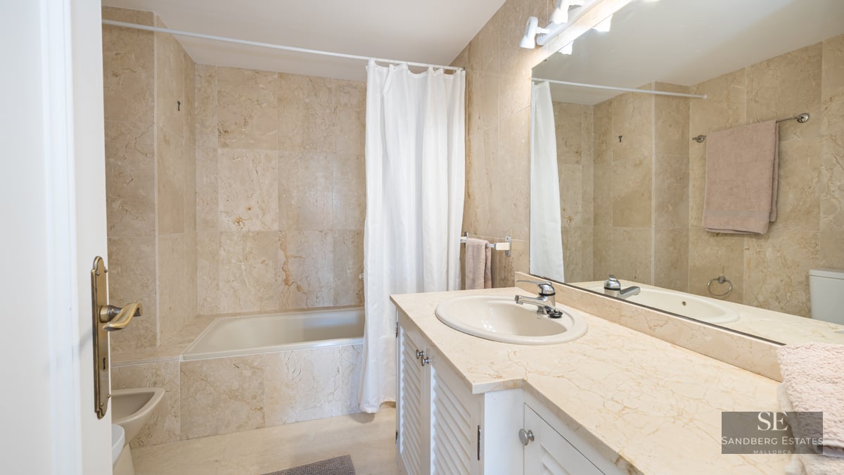 Bathroom featuring beige marble walls, a large mirror, white vanity with marble top, and a bathtub.