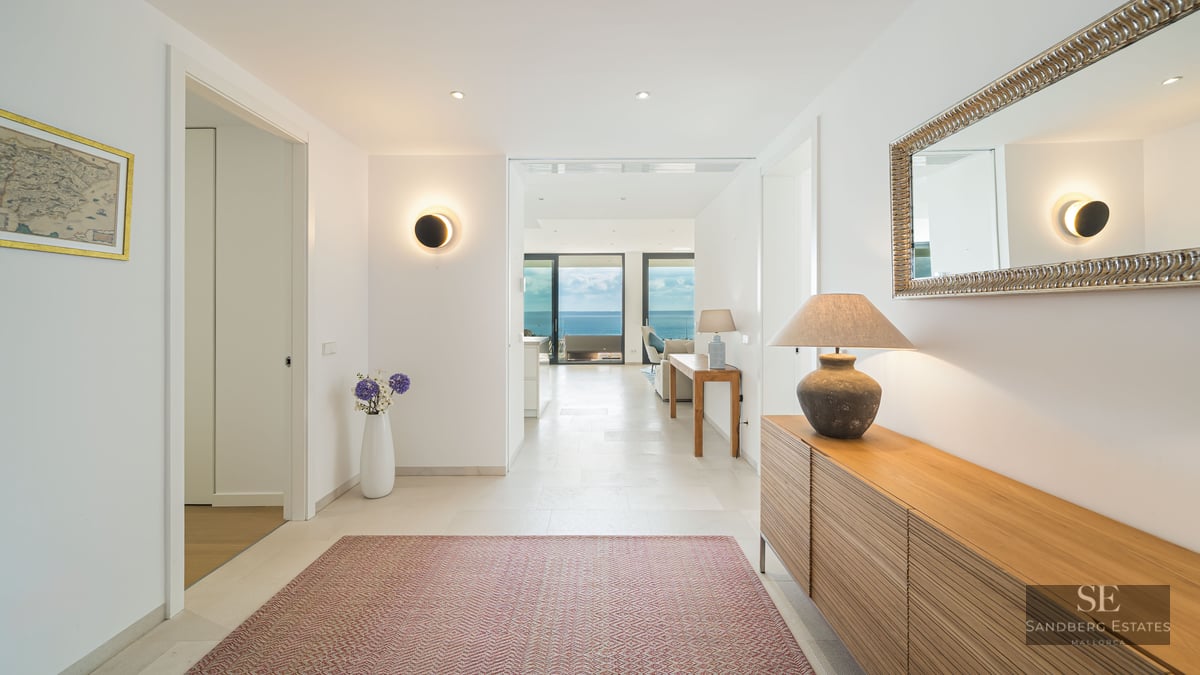 Bright minimalist hallway with wooden furniture and a large mirror, leading to a living room with panoramic ocean views.