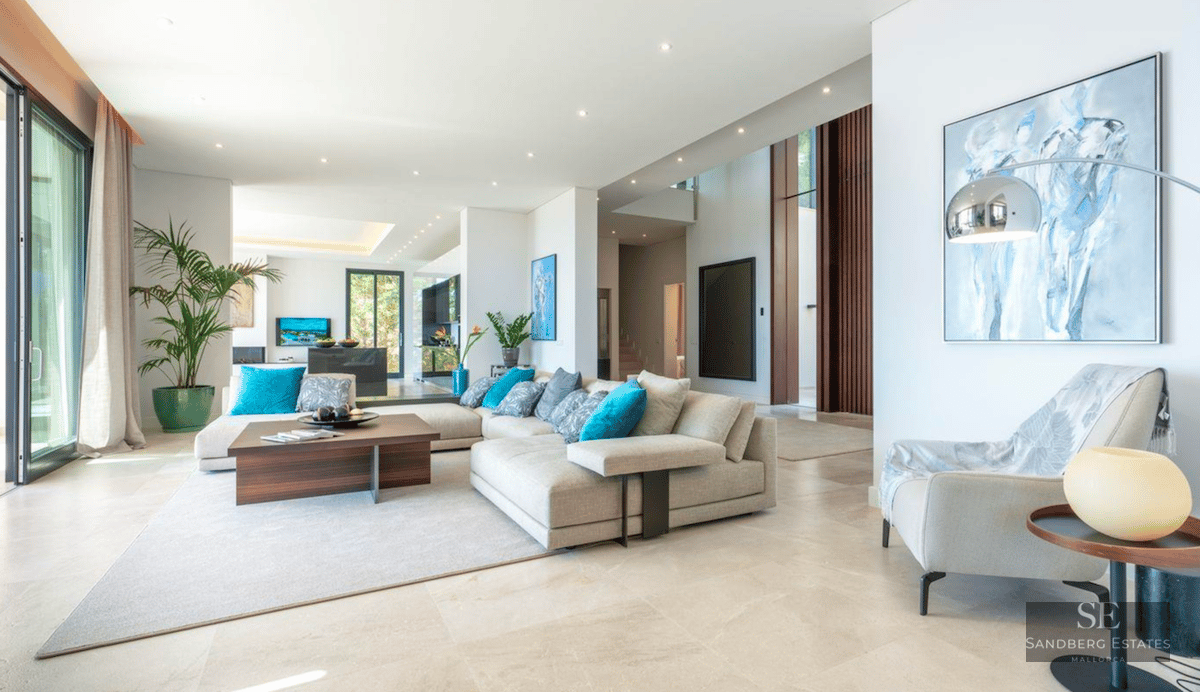 Bright living room with a large beige sectional sofa, turquoise pillows, marble floors, and floor-to-ceiling windows.