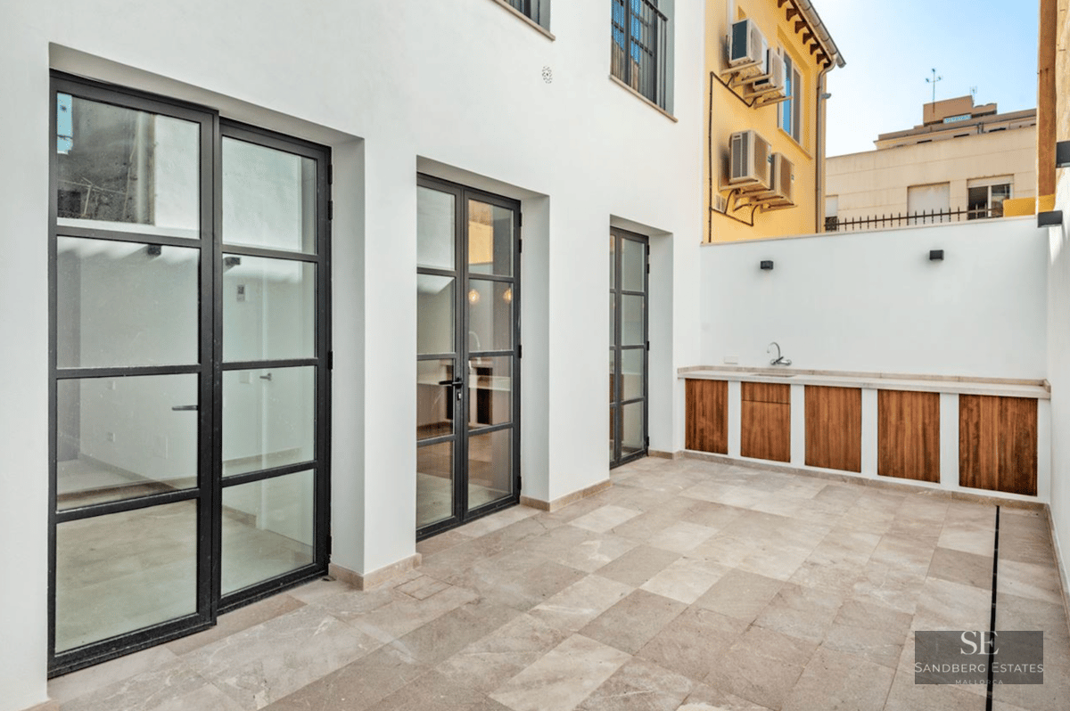 Modern terrace featuring stone tiling, black industrial glass doors, and a wood-accented outdoor kitchen unit.