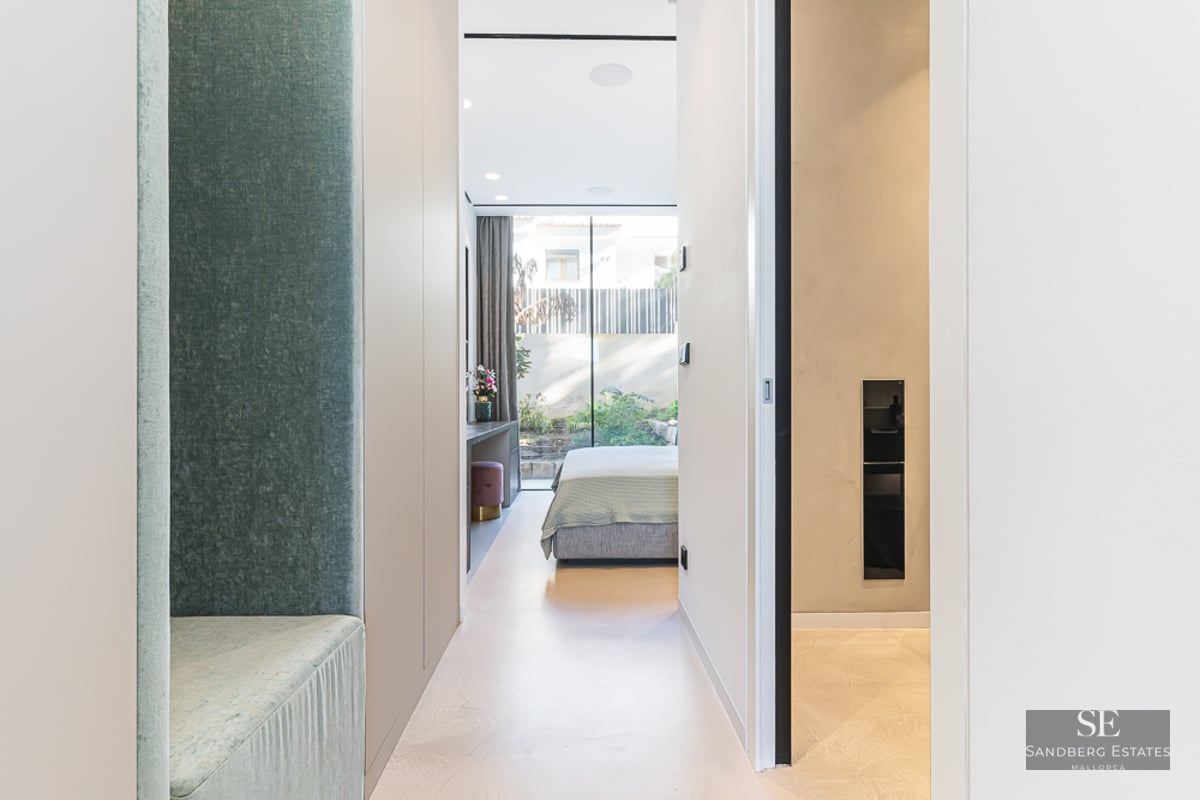 Minimalist hallway leading to a bright bedroom with floor-to-ceiling windows and outdoor garden views.