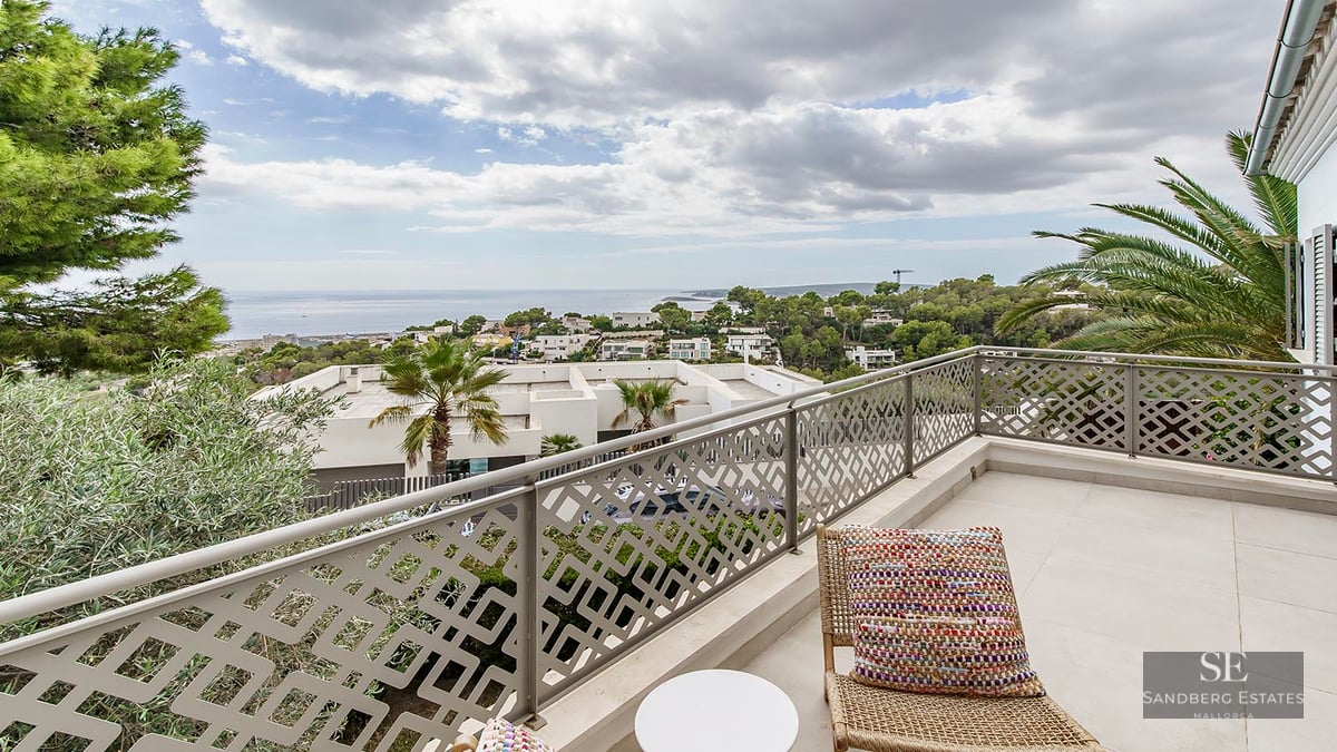 Modern balcony with decorative patterned railing, wicker chair, and views of the Mediterranean coast under a cloudy sky.