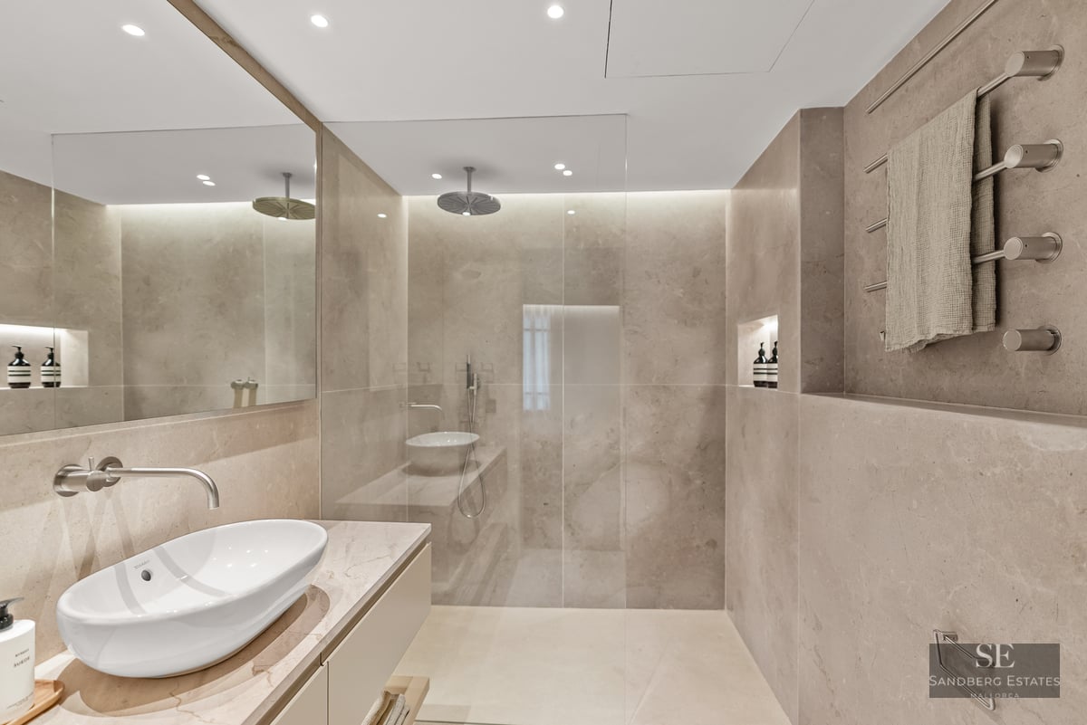 Minimalist master bathroom with beige stone walls, walk-in glass shower, vessel sink, and large mirror.