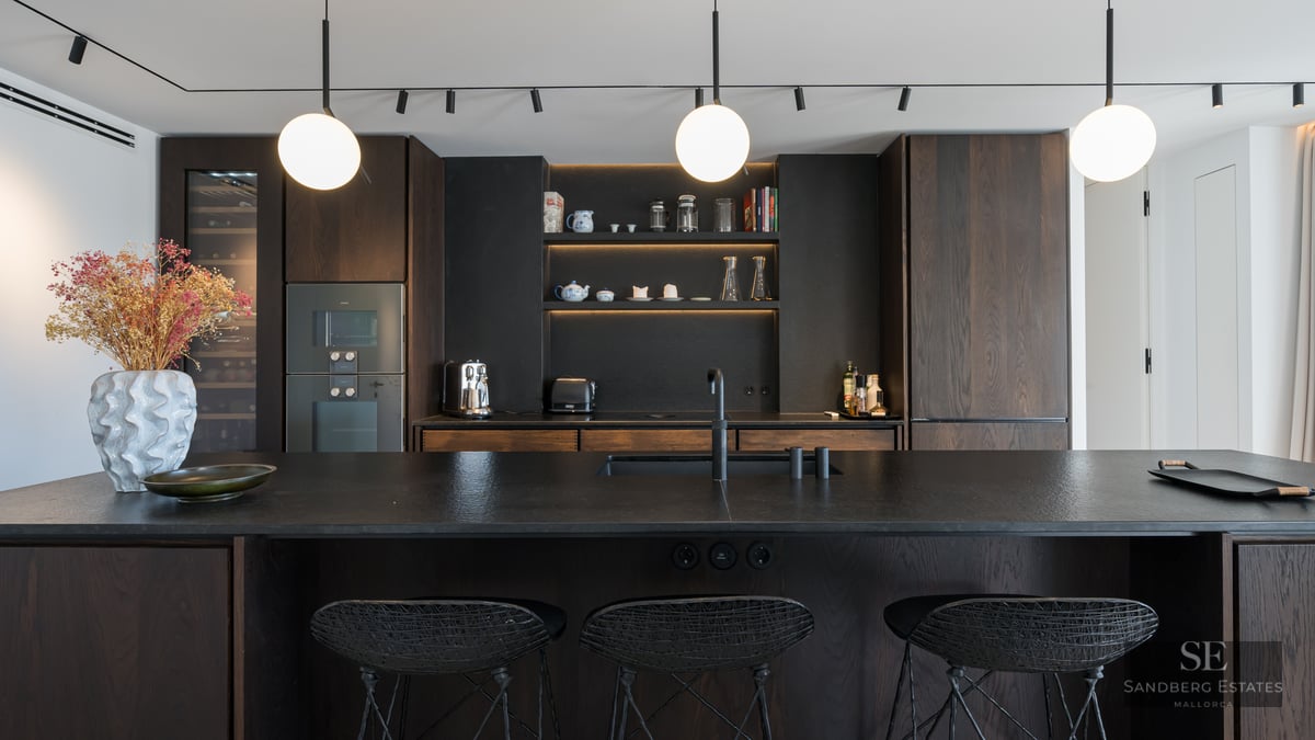 Modern kitchen featuring dark wood cabinets, a black textured island with bar stools, and spherical pendant lights.