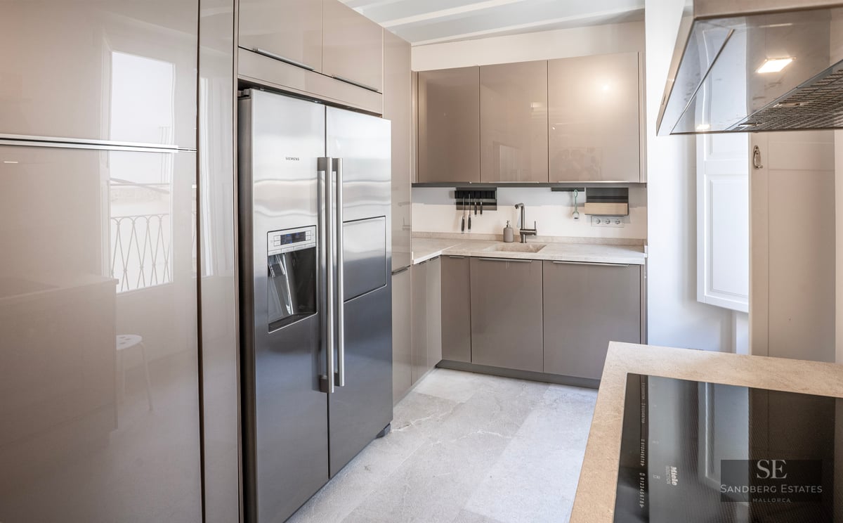 Cuisine moderne avec placards taupe brillant, réfrigérateur en acier inoxydable et plans de travail en pierre claire.