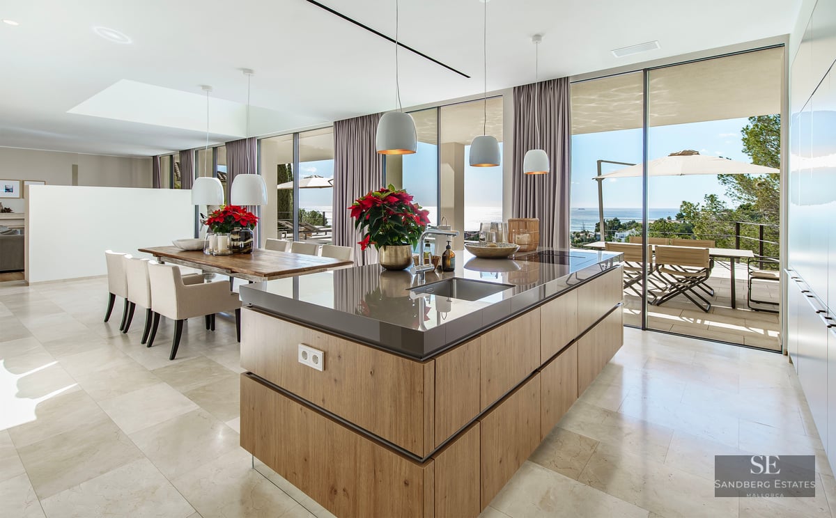 Modern kitchen featuring a wooden island, marble floors, and floor-to-ceiling glass walls overlooking the sea.