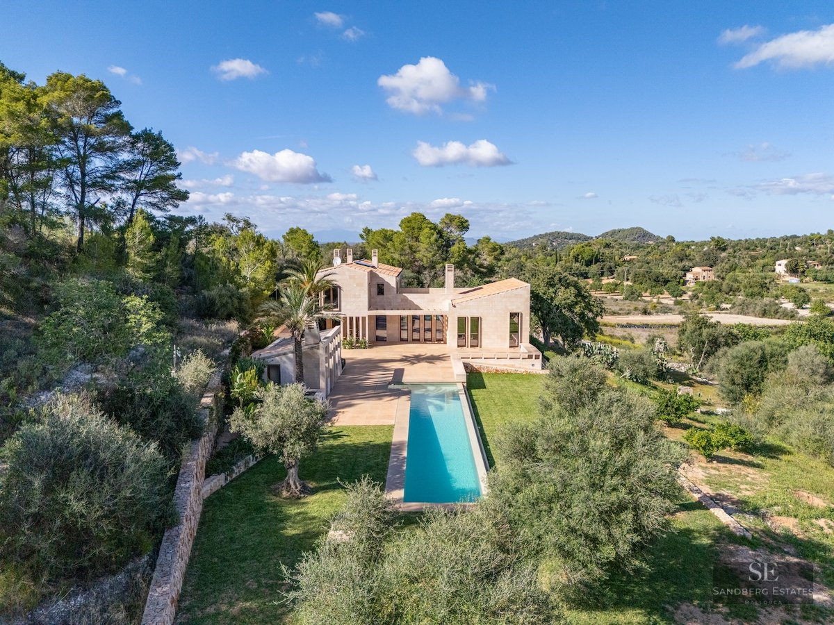Aerial-style view of a modern stone villa with a long turquoise lap pool surrounded by lush Mediterranean trees.