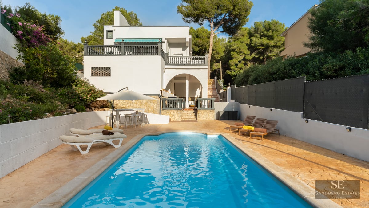 Piscine bleue entourée d'une terrasse en pierre avec transats et une villa blanche en arrière-plan.