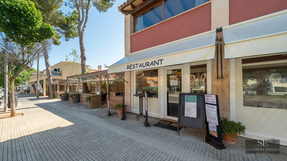 Exterior view of a restaurant with stone walls, white awnings, and a tree-lined sidewalk under a clear sky.