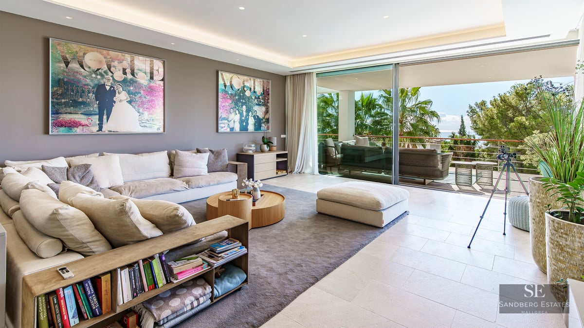 Salon contemporain spacieux avec canapés, art moderne et baies vitrées s'ouvrant sur une terrasse avec palmiers.