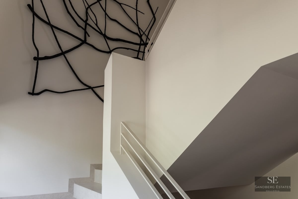 White minimalist staircase featuring a black branch-like art sculpture on the ceiling and walls in a bright, modern space.