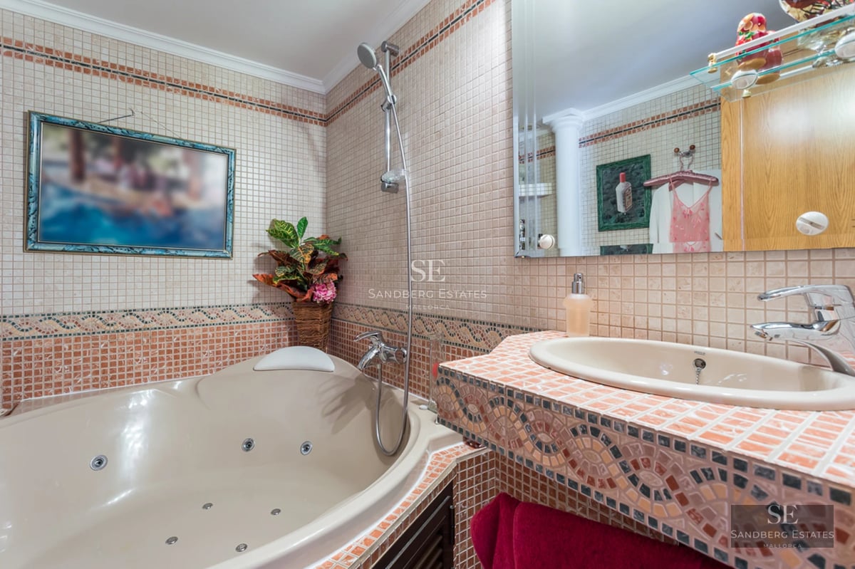 A bathroom with a whirlpool tub, a mosaic-tiled vanity with a sink, and warm-toned wall tiles.
