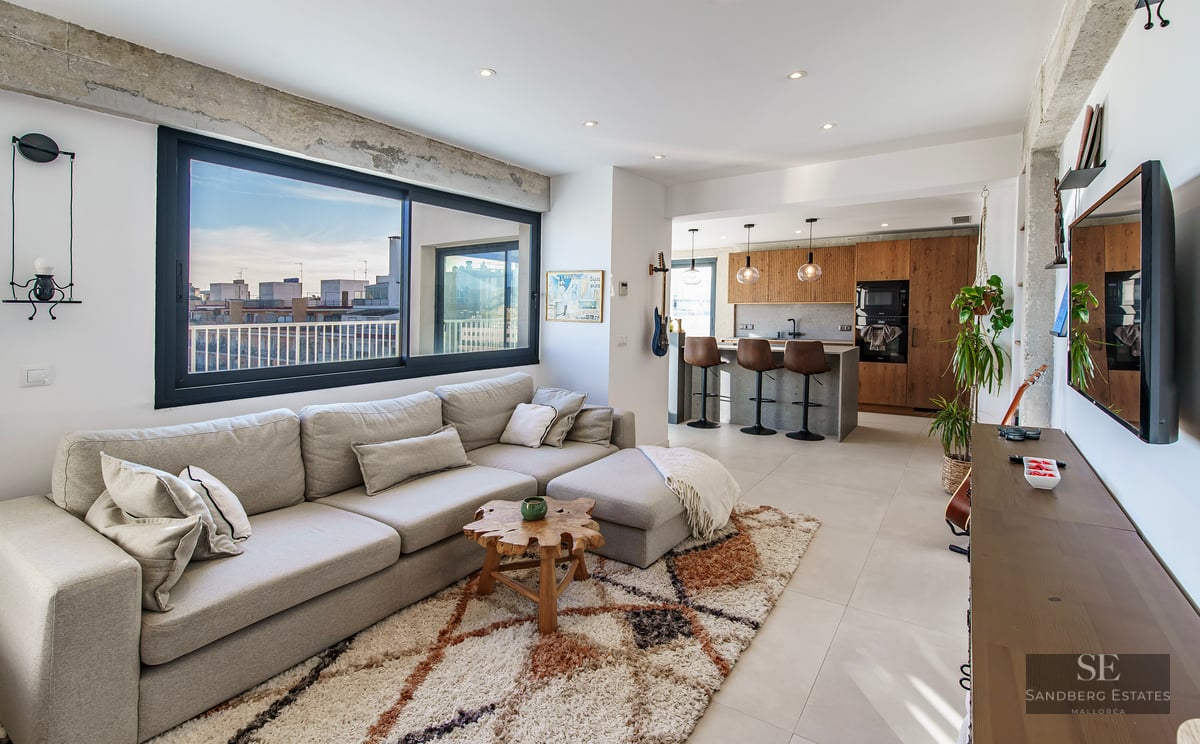 Bright modern living room with a large gray sectional sofa, textured rug, and an open kitchen with city views.