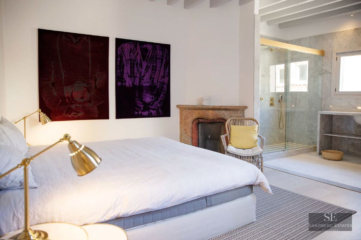 Contemporary master bedroom featuring a rustic fireplace, marble ensuite shower, and elegant brass lighting.