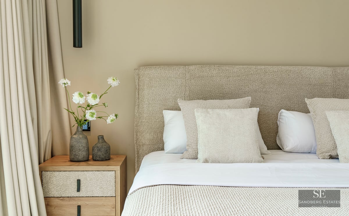 Close-up of a luxury bed with textured headboard, wooden nightstand, and decorative vases with white flowers.