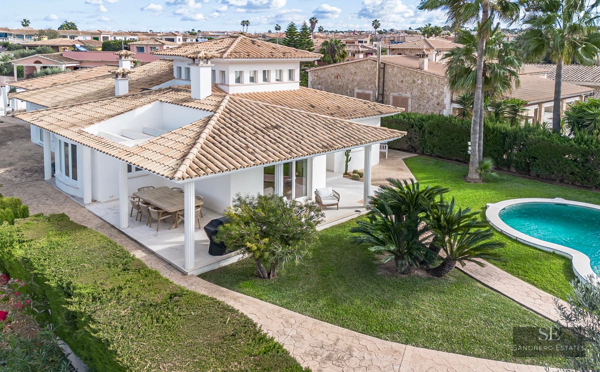 Aerial view of a white Mediterranean villa with terracotta roof, swimming pool, and lush green lawn.