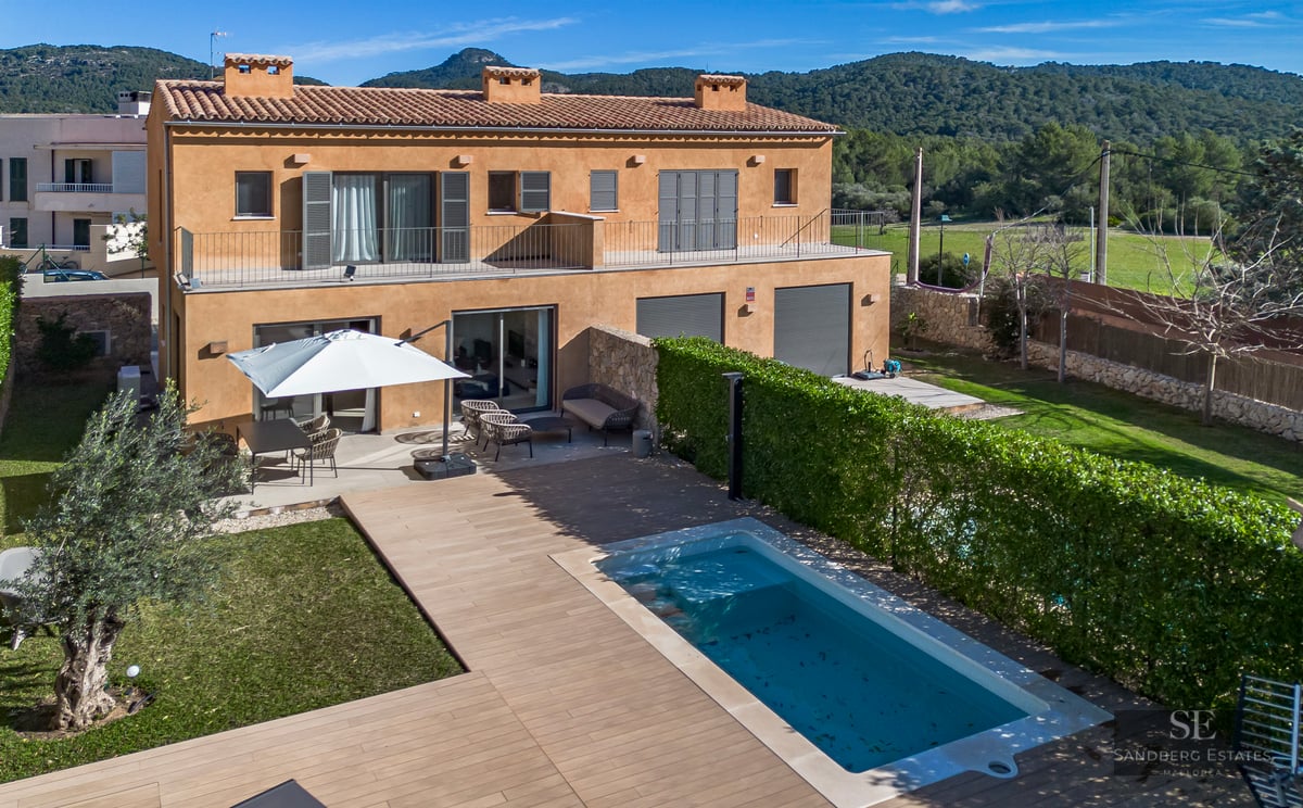 Aerial view of an ochre-colored villa featuring a swimming pool, wooden deck, garden, and hills in the background.