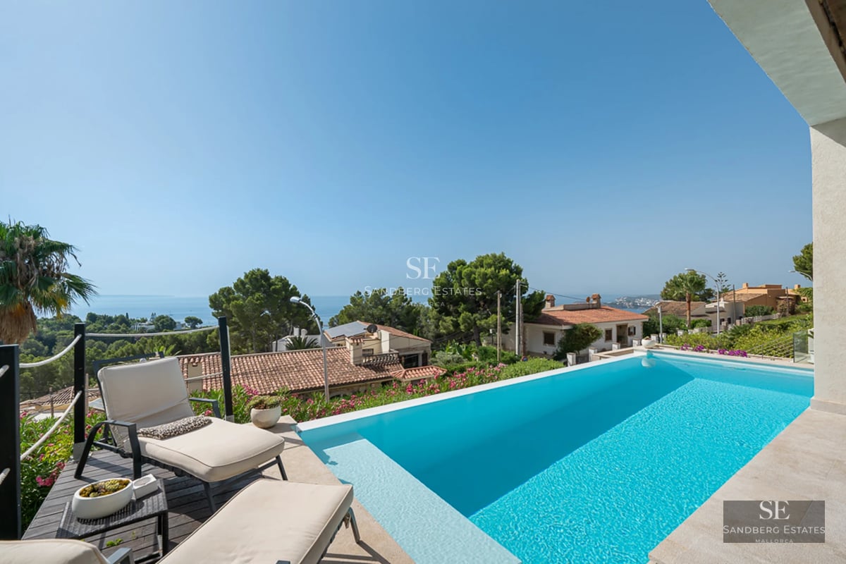 View of a luxury villa with infinity pool, sun loungers, and lush garden. Modern design featuring large windows.