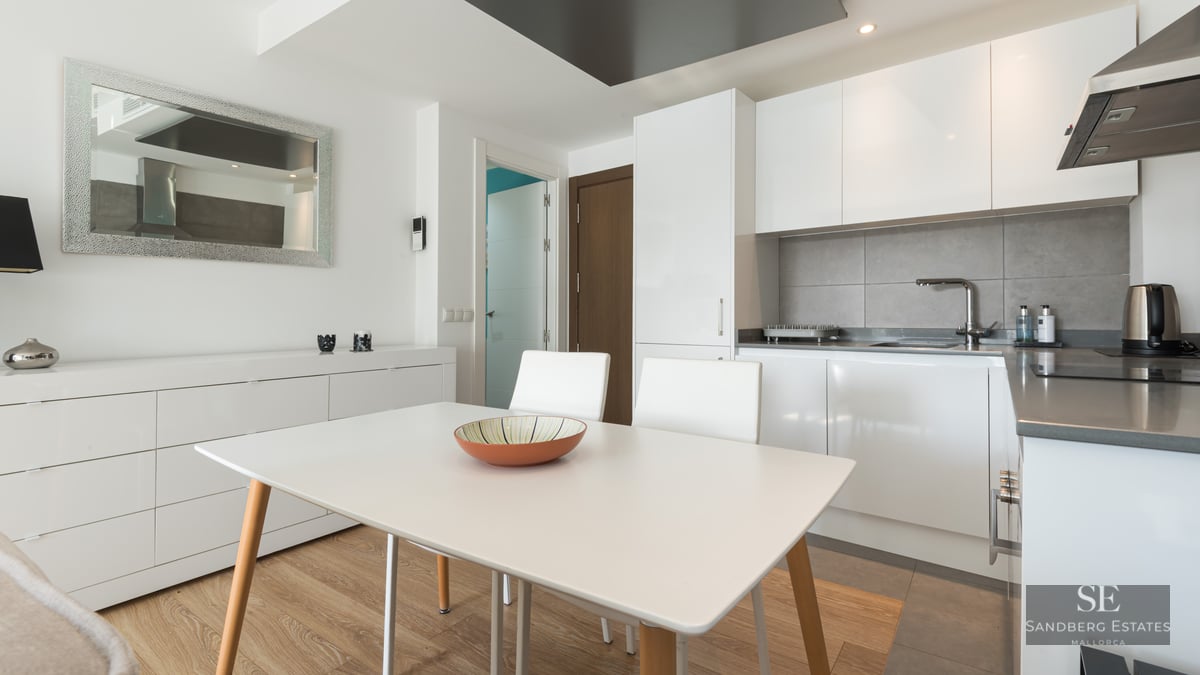 Cuisine moderne lumineuse avec des placards blancs, une crédence grise et une table à manger blanche.