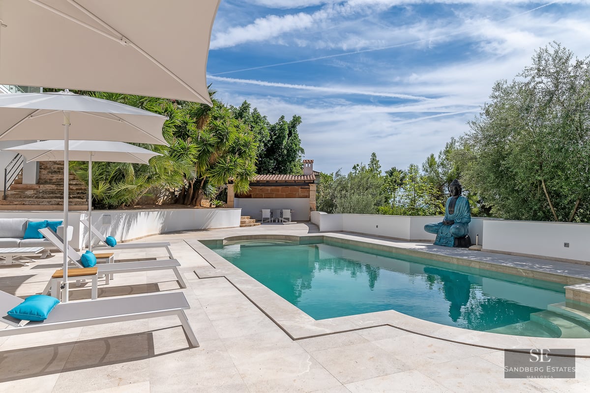 Modern turquoise swimming pool with grey sun loungers, white umbrellas, and a large blue Buddha statue.