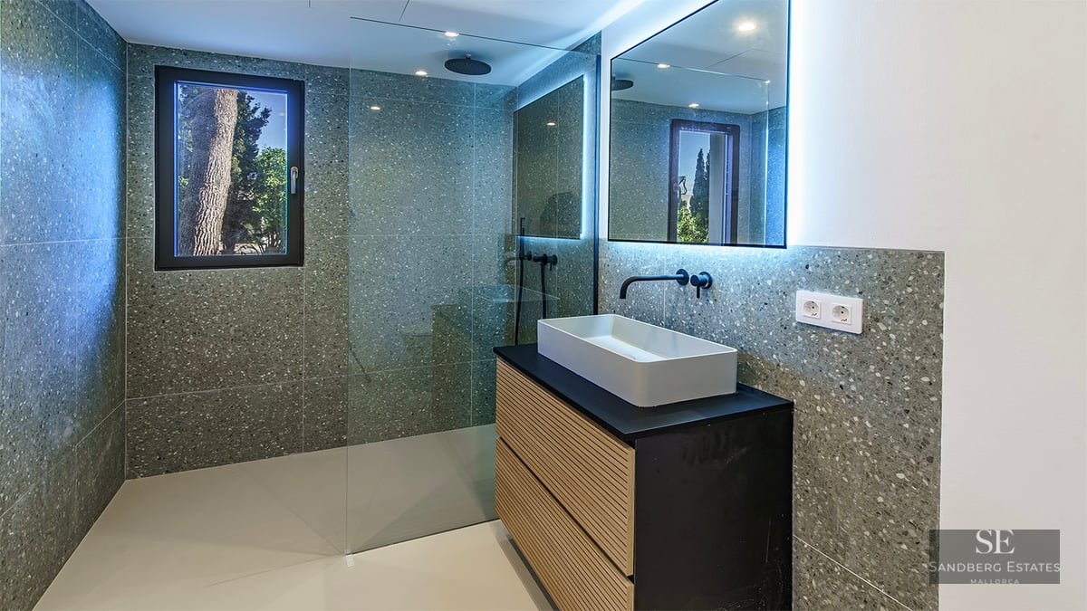 Modern bathroom with grey terrazzo walls, a walk-in glass shower, black fixtures, and a wooden vanity with a white sink.