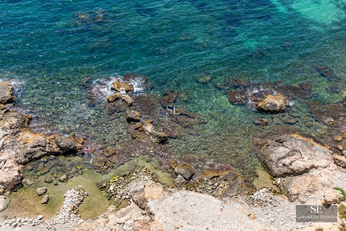 Exterior of modern villa featuring infinity pool, sun loungers, and panoramic Mediterranean sea views. Minimalist architecture and manicured landscaping.