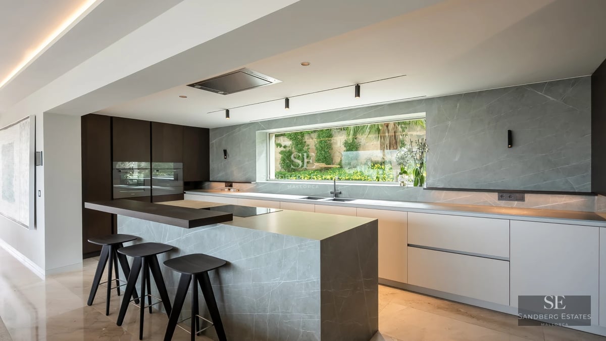 View of an infinity pool with sun loungers, a wooden deck, and a modern house with large windows. Luxury and tranquility.