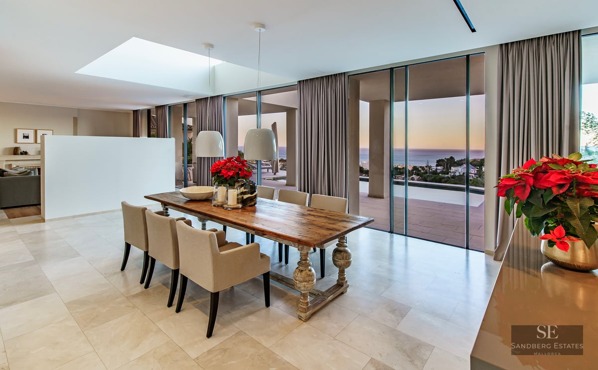 Elegant dining area featuring a long wooden table and floor-to-ceiling windows overlooking the ocean at sunset.