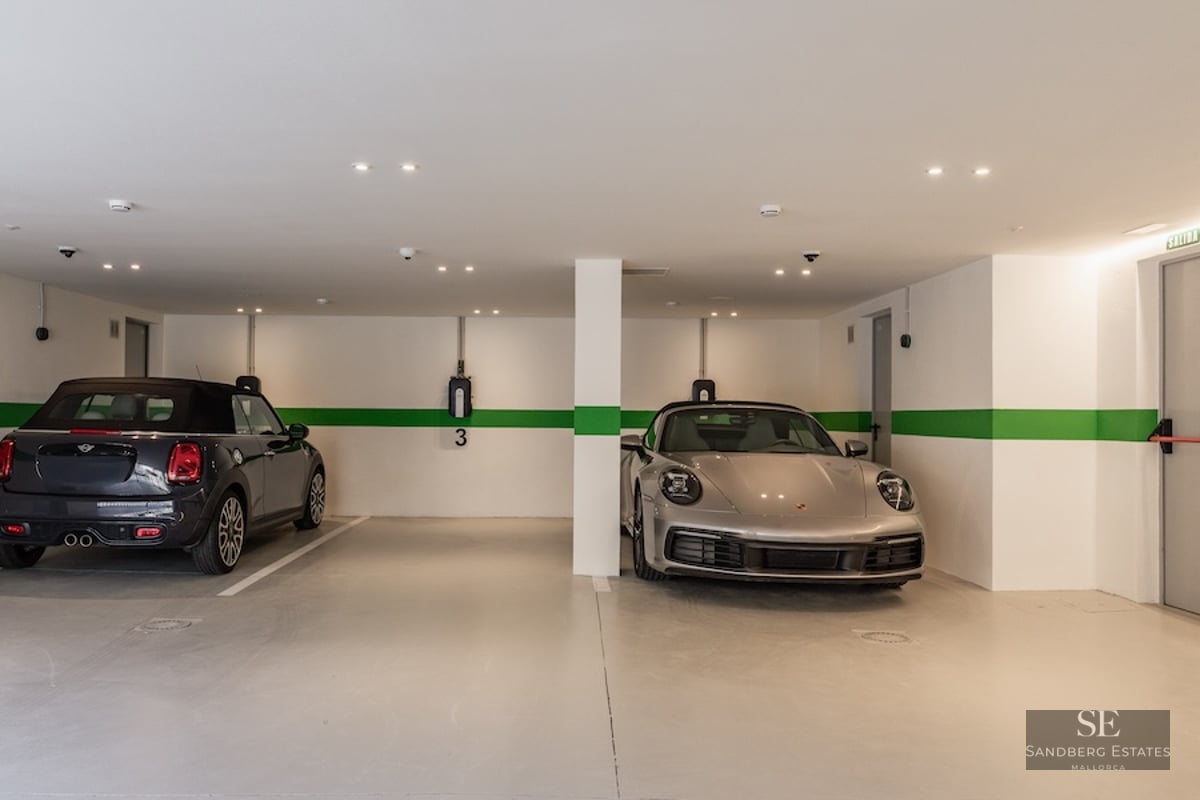 Modern underground parking garage with white walls, green stripes, two cars, and electric vehicle charging points.