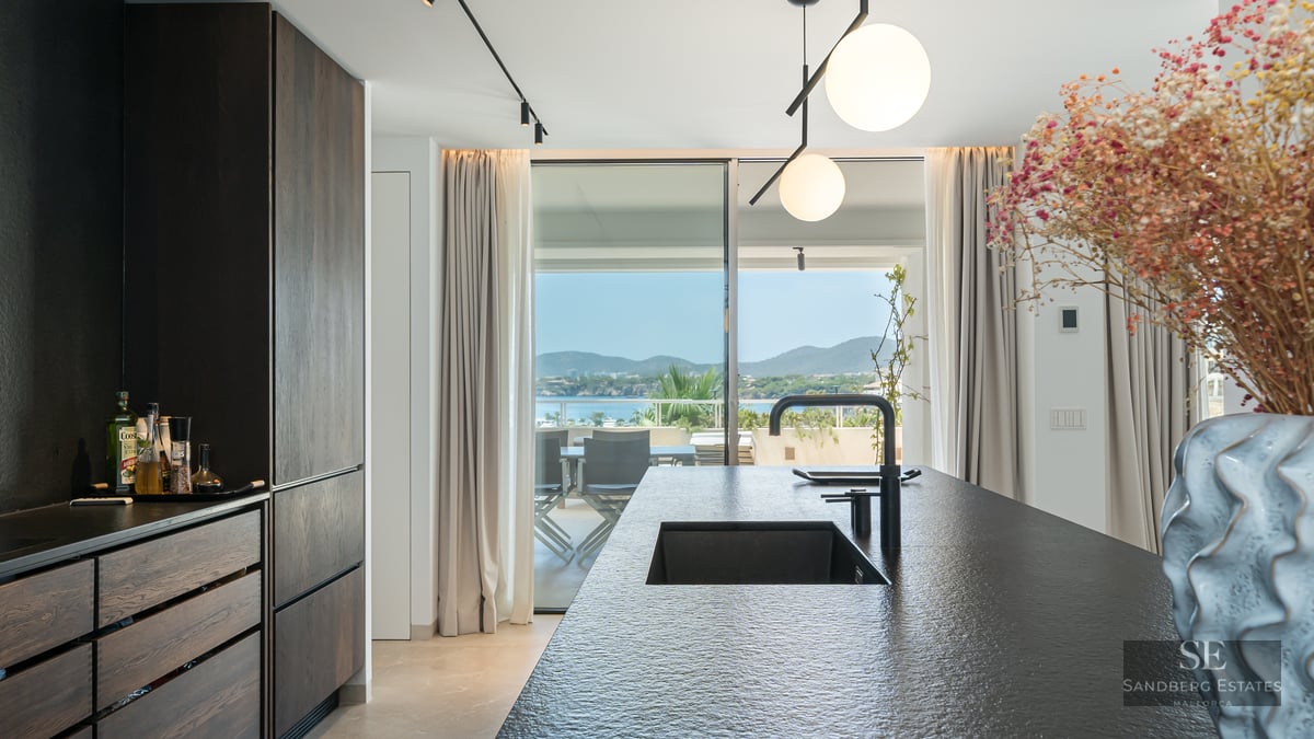 Modern kitchen with a dark stone island and black sink looking out to a sunlit terrace and sea view.