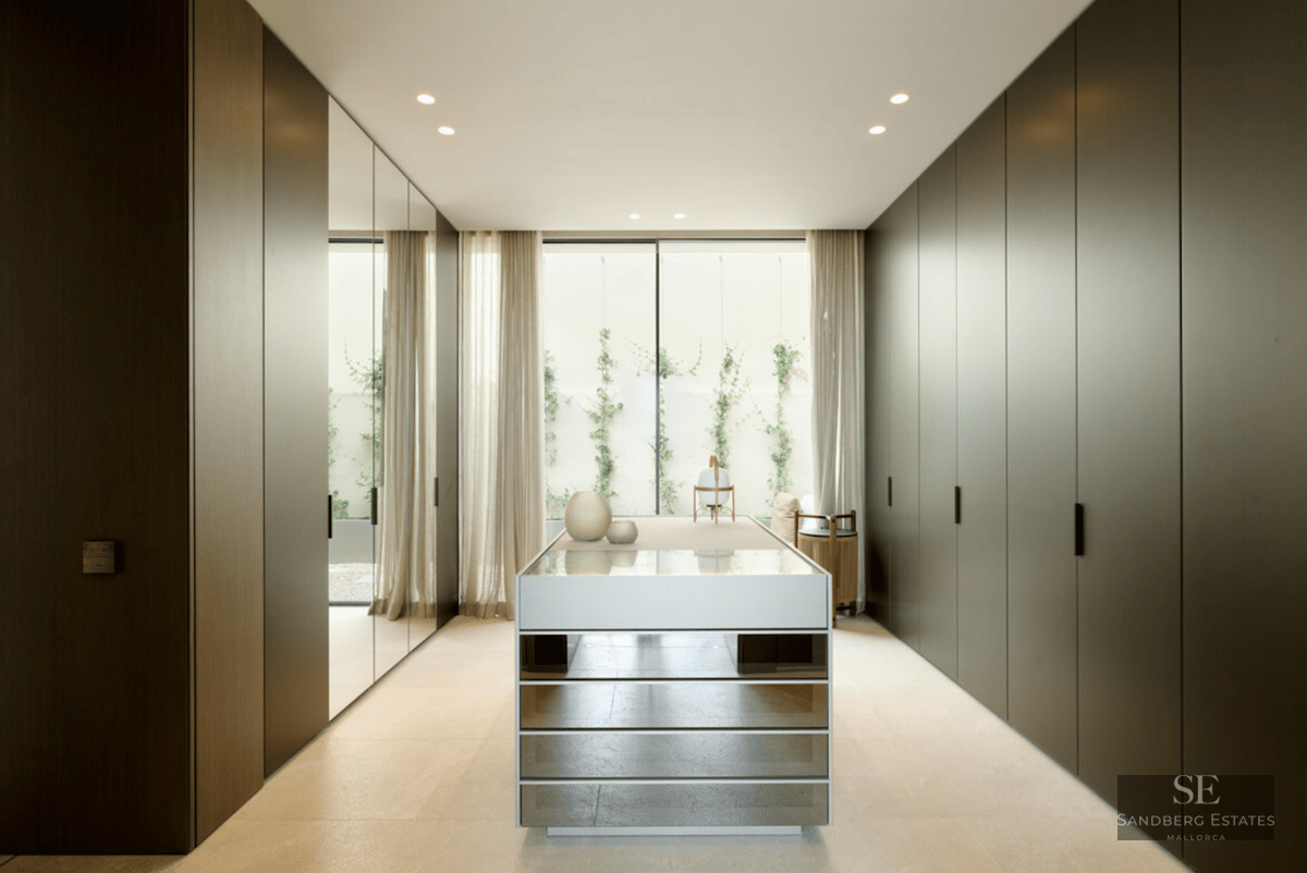 Modern walk-in closet with dark floor-to-ceiling cabinets, a mirrored island, and a garden window.