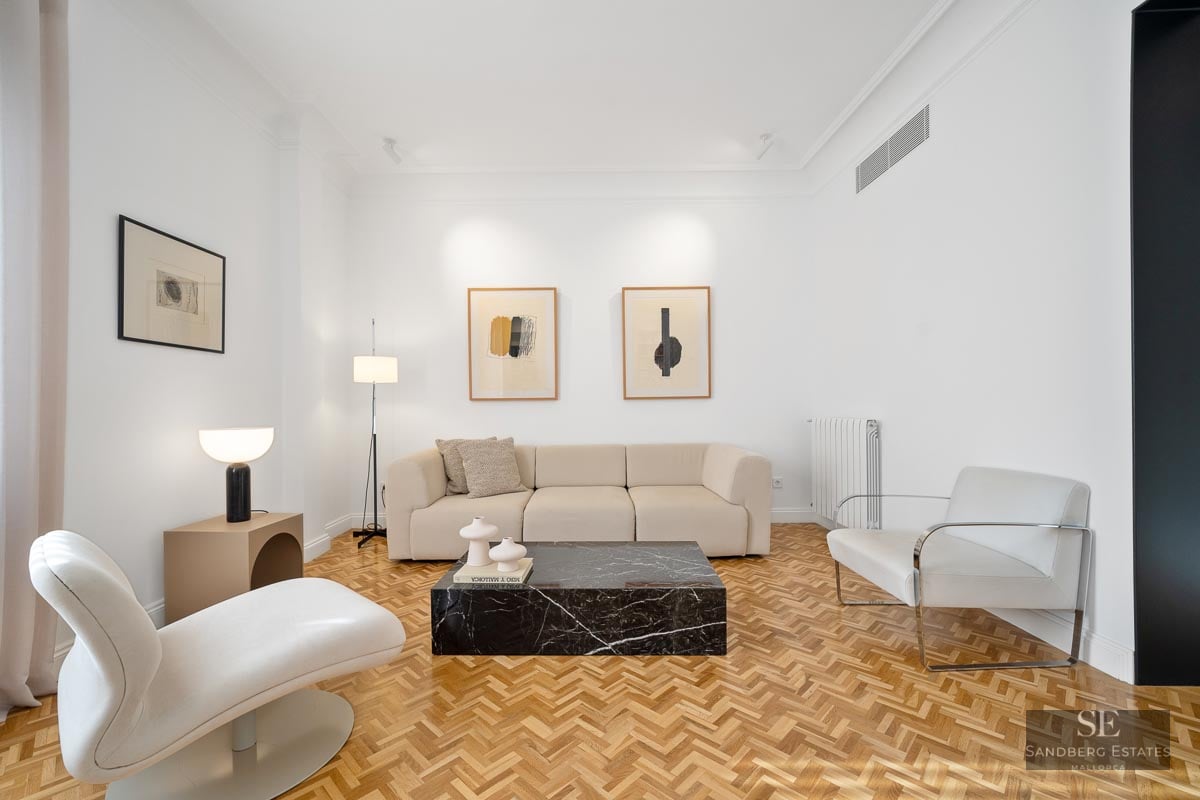 Bright living room with white walls, herringbone wood floor, beige sofa, and a striking black marble coffee table.