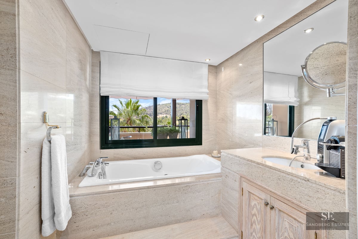 Salle de bain principale élégante avec baignoire en pierre, grande fenêtre avec vue et vasque en marbre.