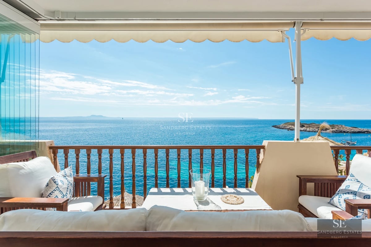 Sun-drenched Mediterranean terrace with white lounge sofas and wooden railing overlooking a sparkling turquoise sea.