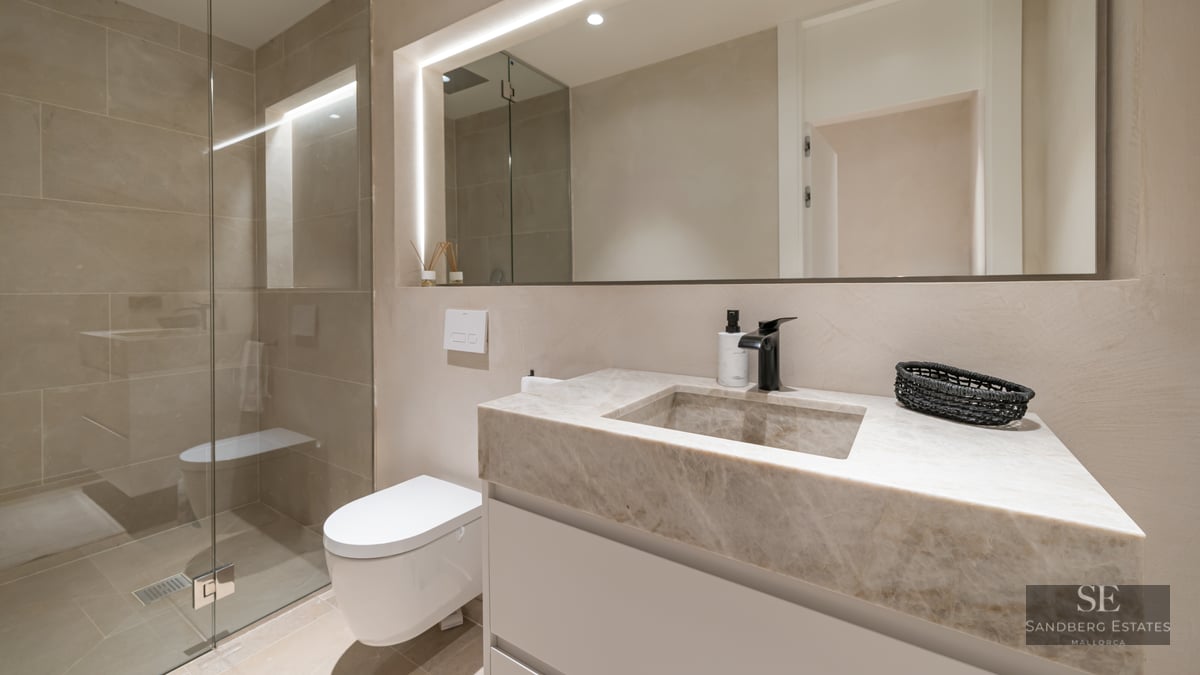 Modern bathroom featuring a stone vanity with integrated sink, black faucet, backlit mirror, and glass walk-in shower.