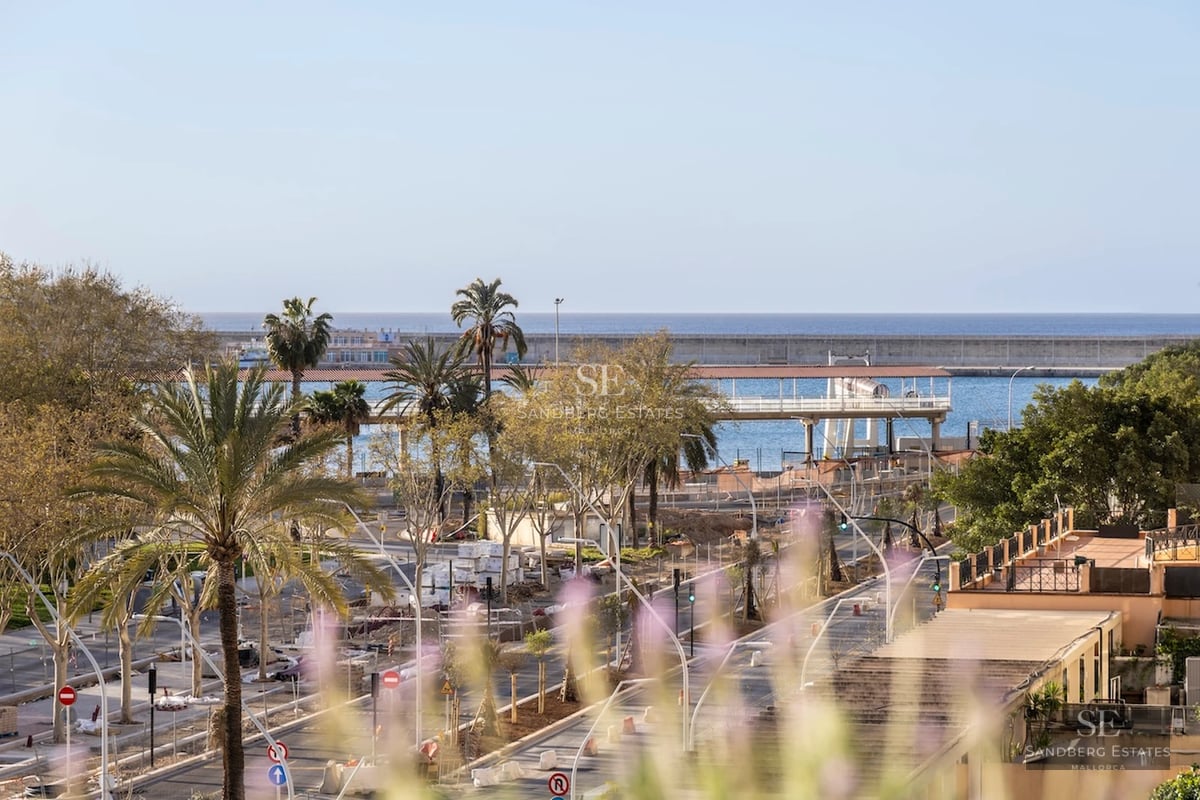 Spacious balcony with a sea view. Wood flooring, glass railing, and modern furniture. Bright and inviting space.