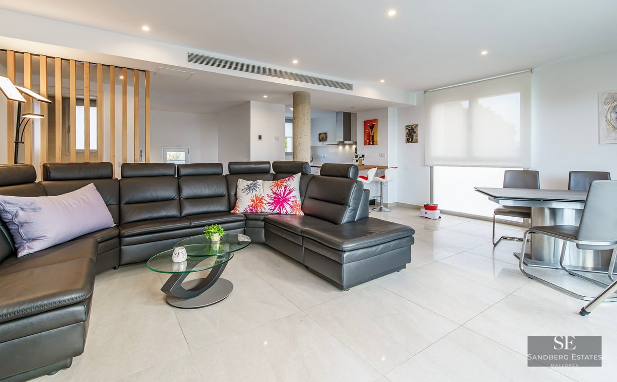 Spacious living room with a large black leather sofa, glass coffee table, and a modern dining area in an open-plan layout.