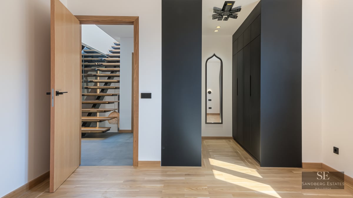 Modern hallway with light wood floors, black built-in closets, and an open door viewing a floating wooden staircase.