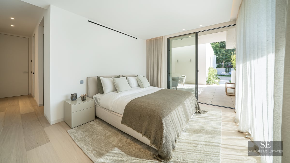 Modern master bedroom featuring a large bed, light wood floors, and sliding glass doors leading to a private terrace.