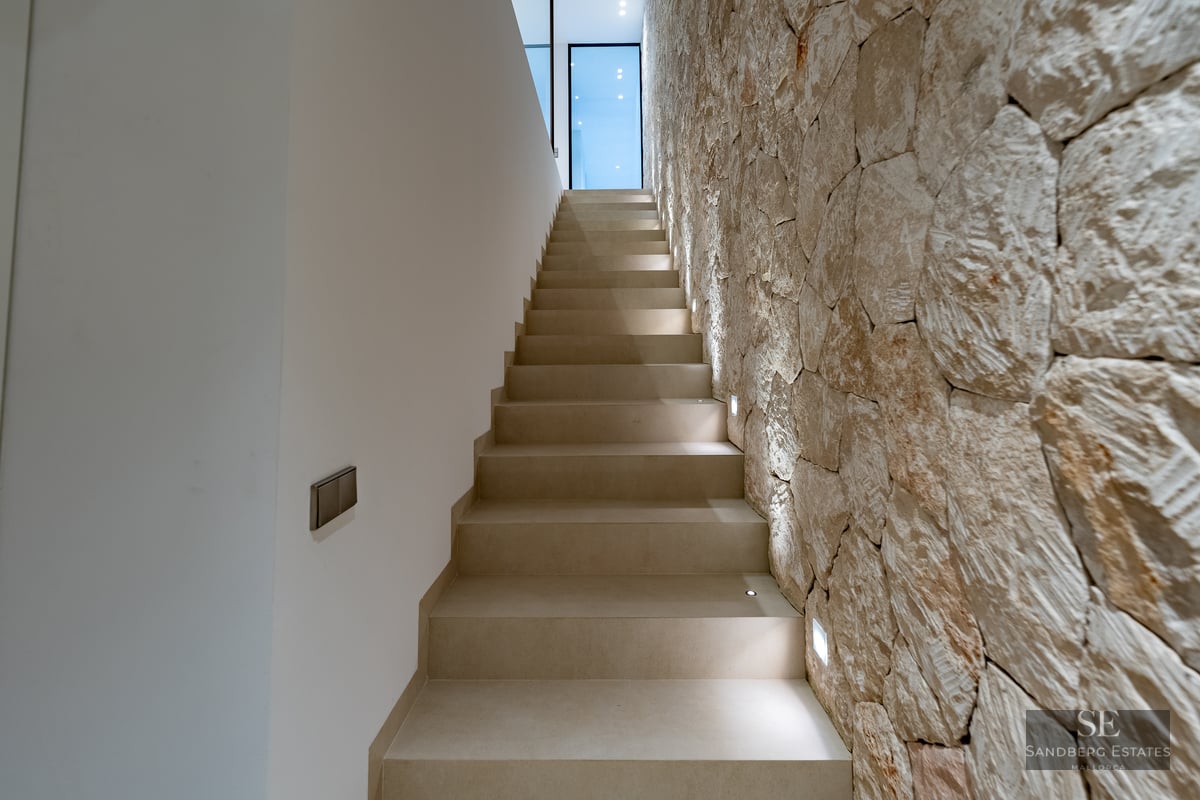 Modern indoor staircase featuring a textured natural stone wall and integrated LED step lighting.