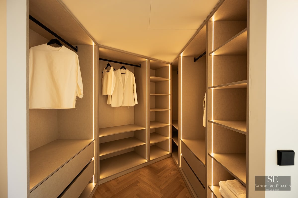 Modern walk-in closet with warm LED strip lighting, light wood cabinetry, and herringbone parquet flooring.