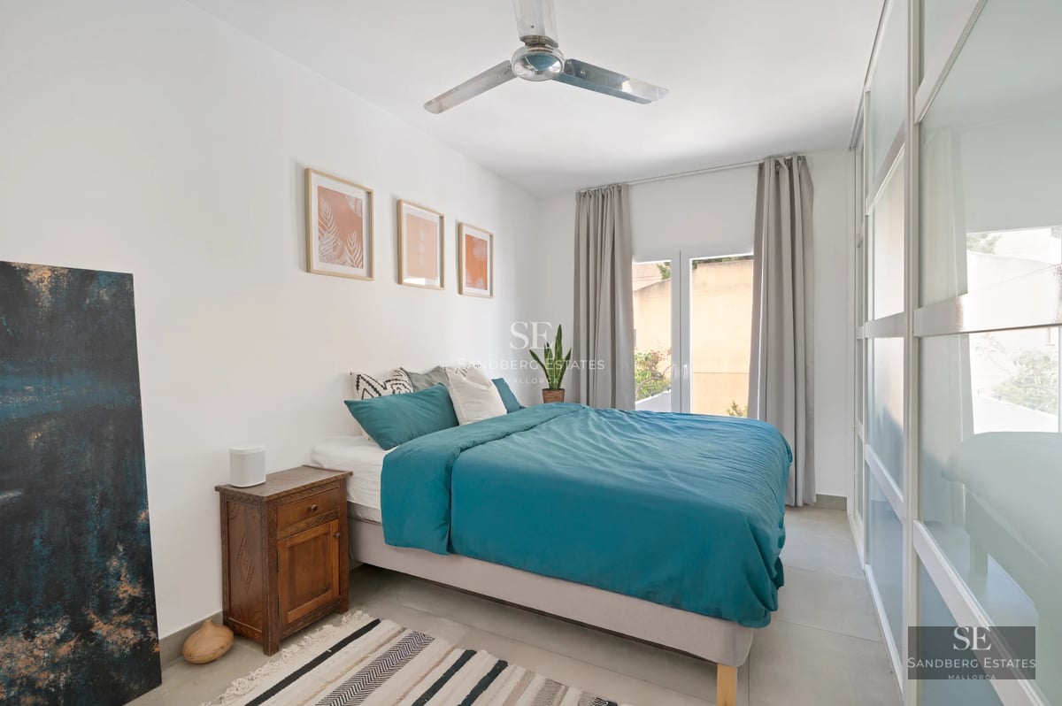 Spacious living room with floor-to-ceiling windows, light wood floors, and modern furniture. Views of lush garden and shimmering pool.