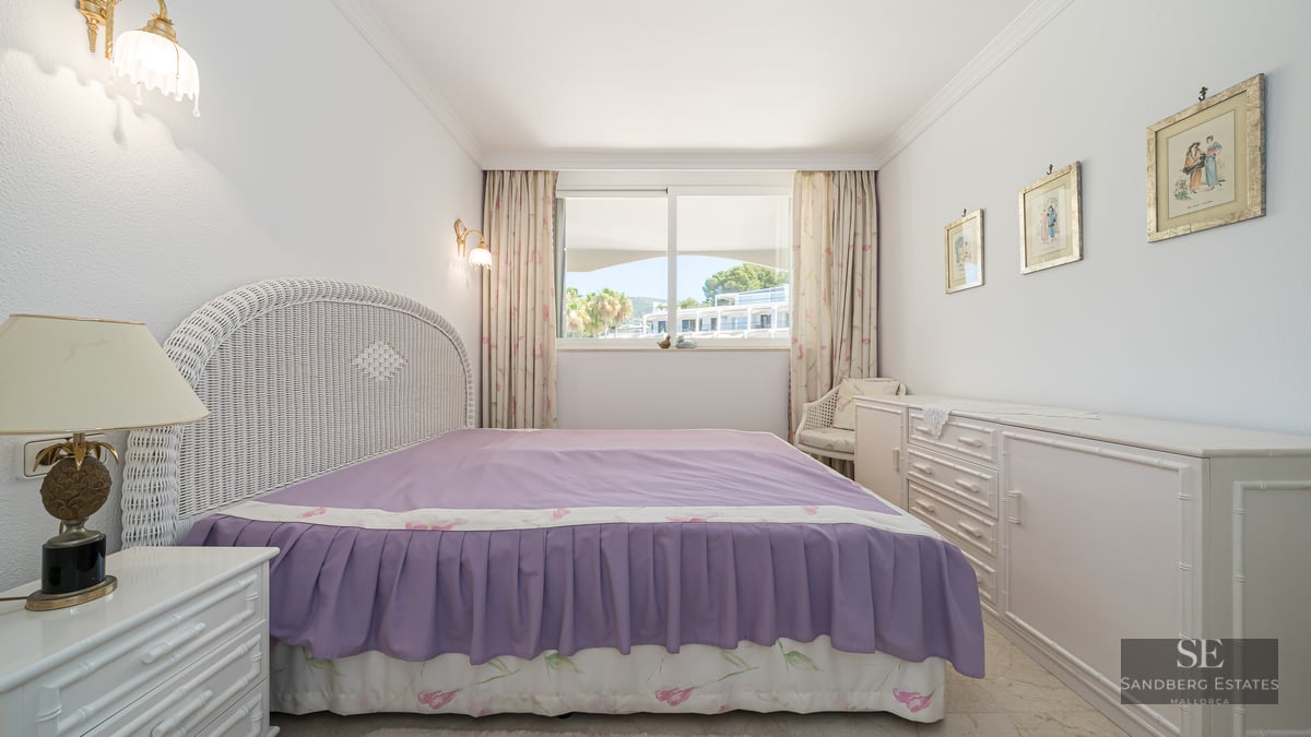 Bedroom featuring a white wicker headboard, purple bedspread, and a large window overlooking a sunny courtyard.
